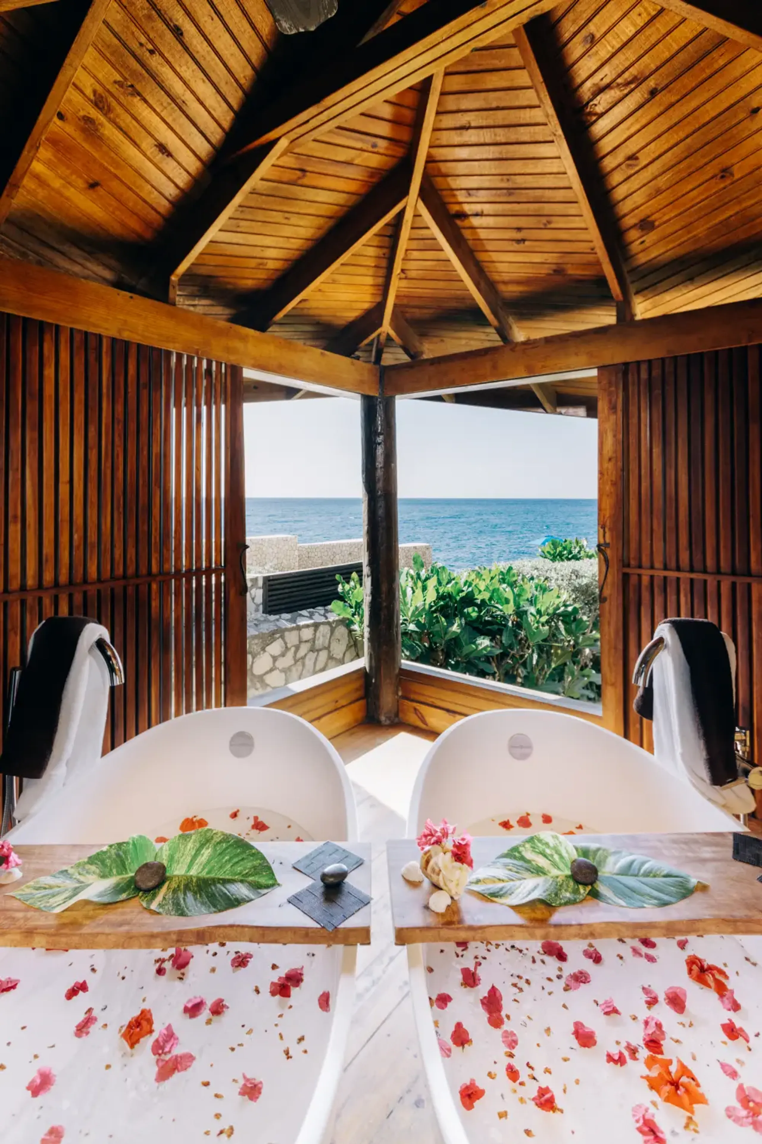 Oceanfront spa sanctuary at Rockhouse Hotel in Negril, Jamaica, featuring side-by-side soaking tubs with flower petals and tropical leaves, offering couples a luxury wellness experience with stunning Caribbean Sea views